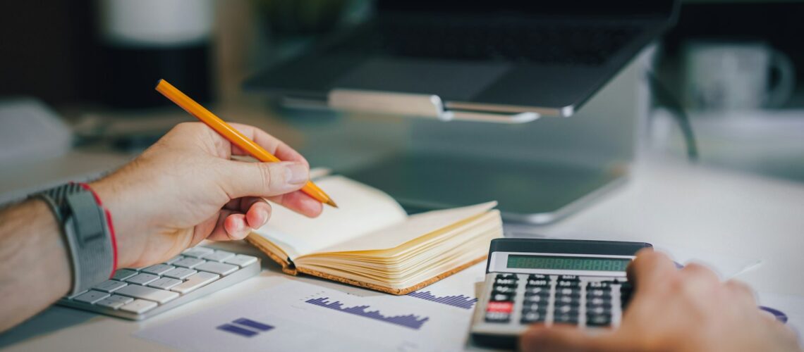 Person working through financial reports with a calculator and notebook