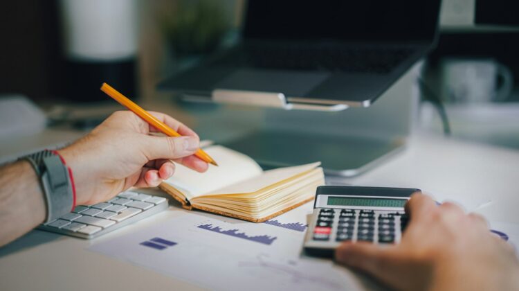 Person working through financial reports with a calculator and notebook